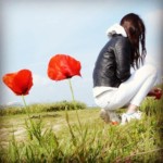 Une jeune fille accroupie à côté de coquelicots.